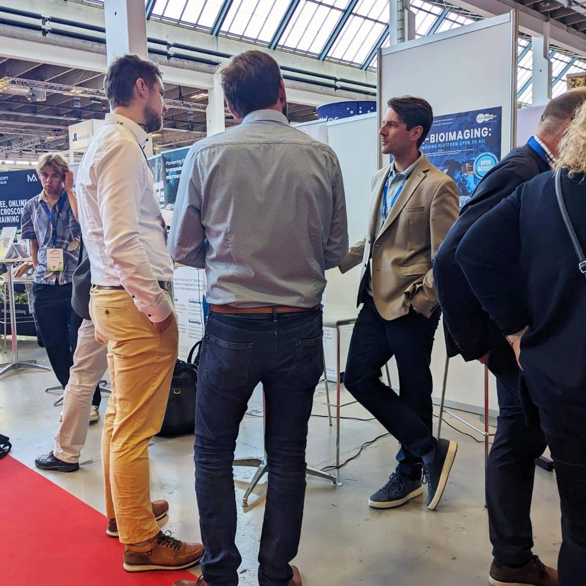 View of the IEM CAS exhibition stand with a height advertising banner and visitors discussing with scientist Štěpán Kortus.