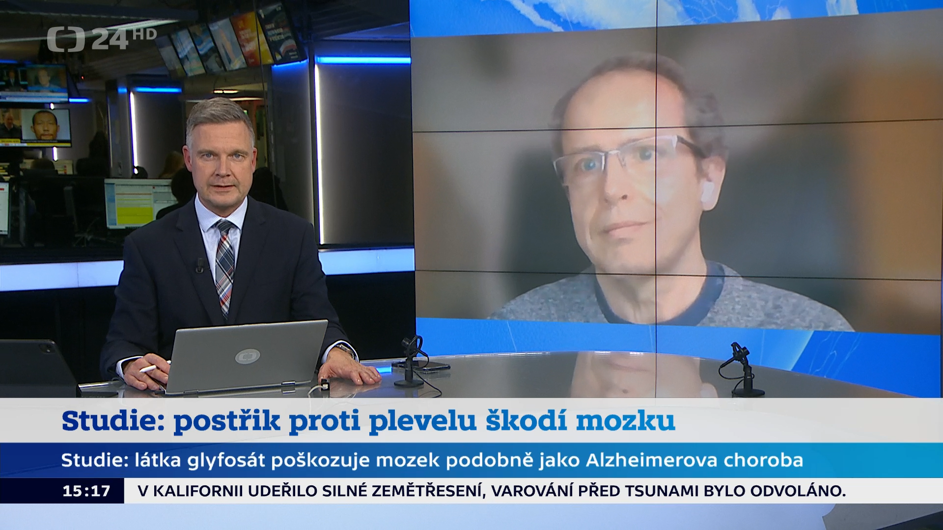 Print screen obrazovky, pohled do studia na moderátora pořadu, vědec Pavel Rössner, který je připojen vzdáleně se zobrazuje na obrazovce napravo od moderátora.